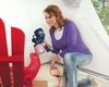 Woman using a handheld HVLP paint sprayer to finish a red wooden chair in a workshop tent