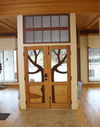 Double wooden doors with decorative tree branch cutouts and glass panels in a workshop setting.