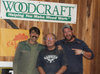 Three men standing in front of Woodcraft banner inside woodworking workshop