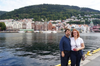 Couple standing by waterfront with sailboats and hillside town in background, no visible woodworking tools or projects.