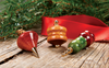 Three turned wooden Christmas ornaments with brass finials on rustic wood, pine branches, and red ribbon background