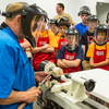 Instructor demonstrating woodturning on a lathe to youth wearing protective face shields and JET aprons.