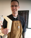 Woodworker wearing apron holding a wooden frame with a dovetail joint in a workshop setting