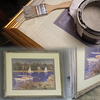 Two picture frames with artwork, one gold frame being painted with a brush and white paint nearby