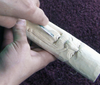 Hands carving detailed facial features on a wooden cane topper using a gouge tool.