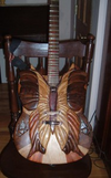 Acoustic guitar with intricate carved wooden butterfly design on body, resting on wooden chair
