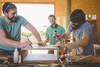 Three men assembling a wooden box with clamps and glue in a bright workshop