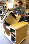 Woodworker installing a Delta planer into a custom plywood cabinet with storage shelves in a workshop