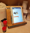 Wooden cookbook or tablet stand with metal braces holding a tablet upright on a kitchen counter
