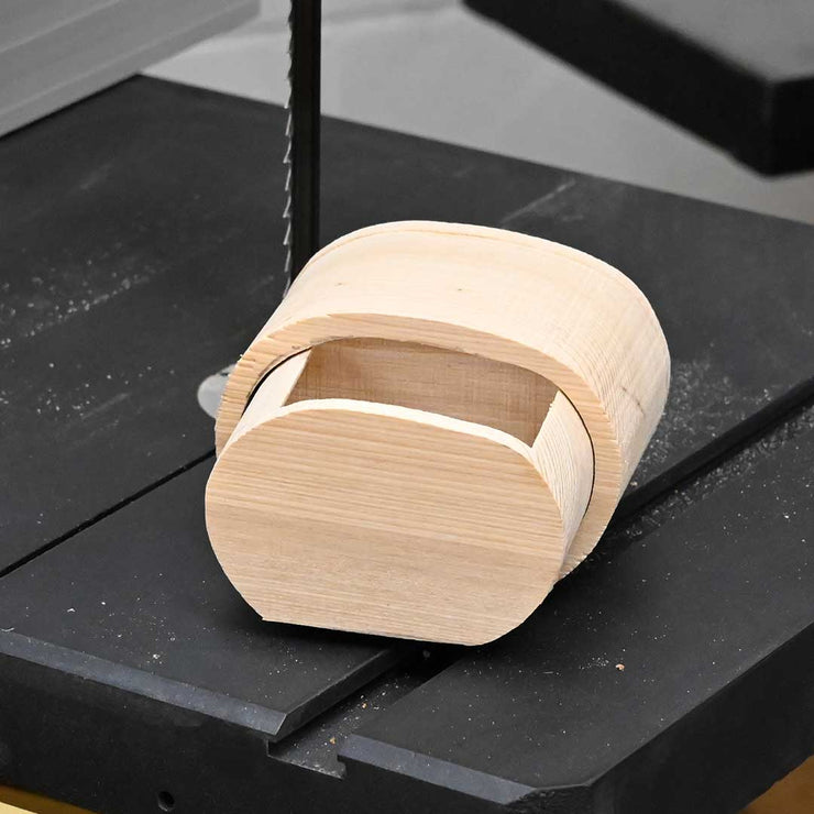 Partially finished wooden bandsaw box displayed on a bandsaw table, showing the cut-out drawer cavity and smooth curved