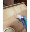 Hand applying light-colored wood finish with brush on blanket chest panels in workshop setting