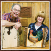 Two woodworkers holding carved wooden panels featuring a rooster and a horse silhouette in a workshop setting