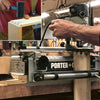 Hands using a Porter-Cable dovetail jig and mallet to assemble machine-cut dovetail joints on wood boards.