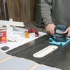 Person using an electric orbital sander to remove rust from a table saw surface in a workshop.